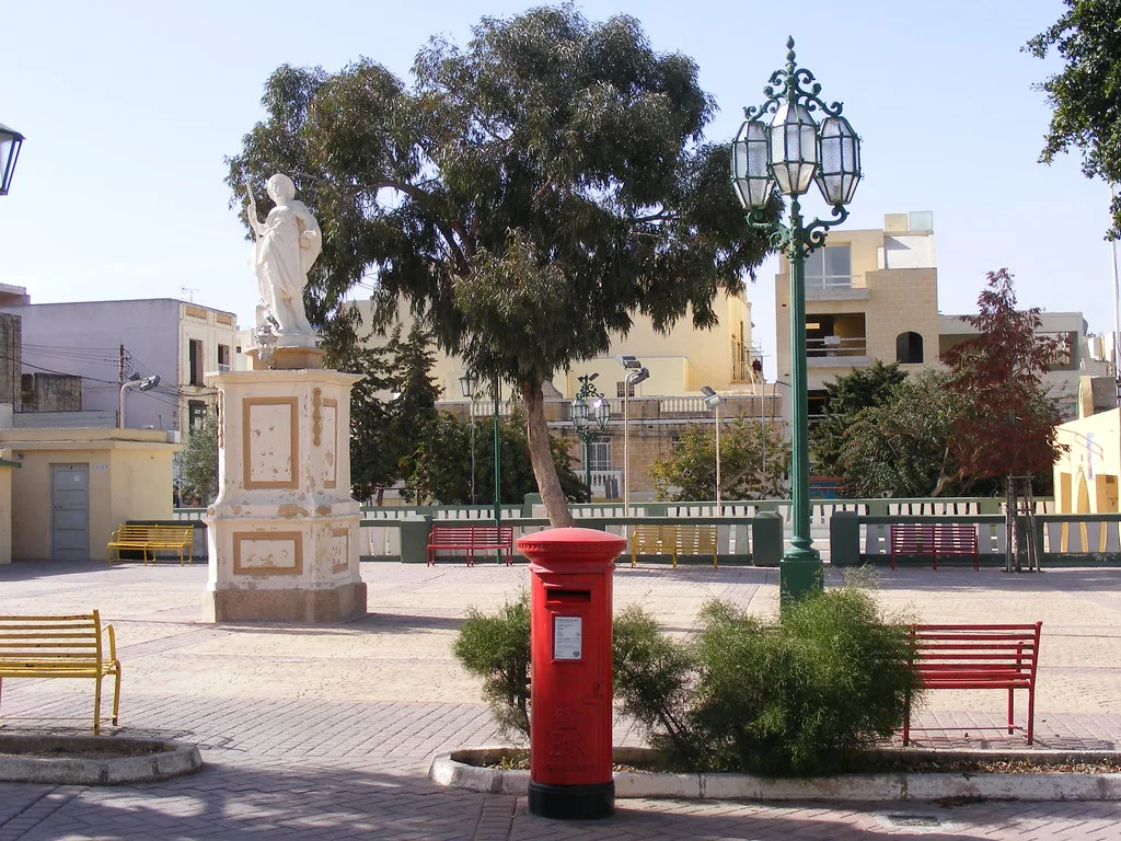 A square with a statue and a red postbox in Għaxaq.