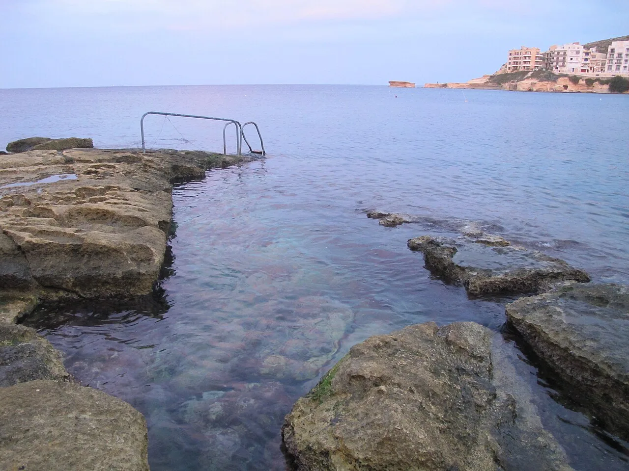 Rock pools and a bathing ladder on the Marsalforn shoreline, Gozo.