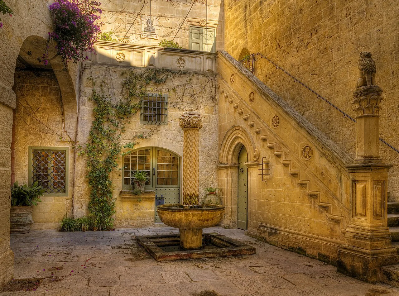 A palazzo courtyard with a stone staircase and fountain in Mdina.